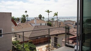 Een balkon met uitzicht op een kuststad, inclusief palmbomen en een brug.