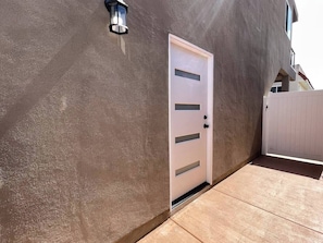 A modern building with a textured facade, a white door with horizontal panels, and a small outdoor area with a light fixture. - Harbor View Haven by Balboa Park (San Diego)