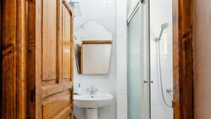 Een houten deur, een wit wasbakje, een spiegel en een glazen douchecabine in een badkamer.
