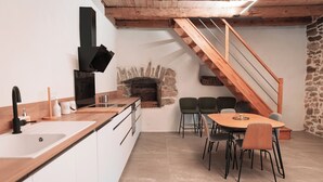 Una cocina moderna con chimenea de piedra, escalera de madera y un comedor con sillas.