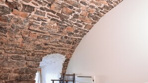 Un dormitorio con pared de piedra, techo curvo, cama con ropa blanca y suelo de madera.