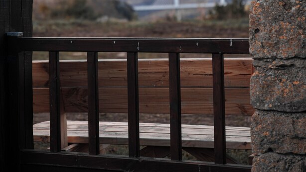 Un banco de madera con un pilar de piedra al frente, con vista a un puente y colinas distantes.