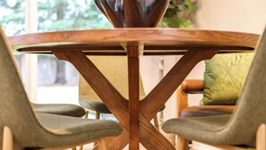 Una mesa redonda de madera con base en forma de cruz, rodeada por tres sillas tapizadas.