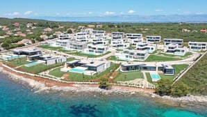 En semesteranläggning vid kusten med moderna villor, en central pool och utsikt över havet och bergen.