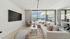 Un salon moderne doté d’un grand téléviseur à écran plat, d’un ensemble de canapés, d’une table basse et d’un coin repas offrant une vue sur la mer.