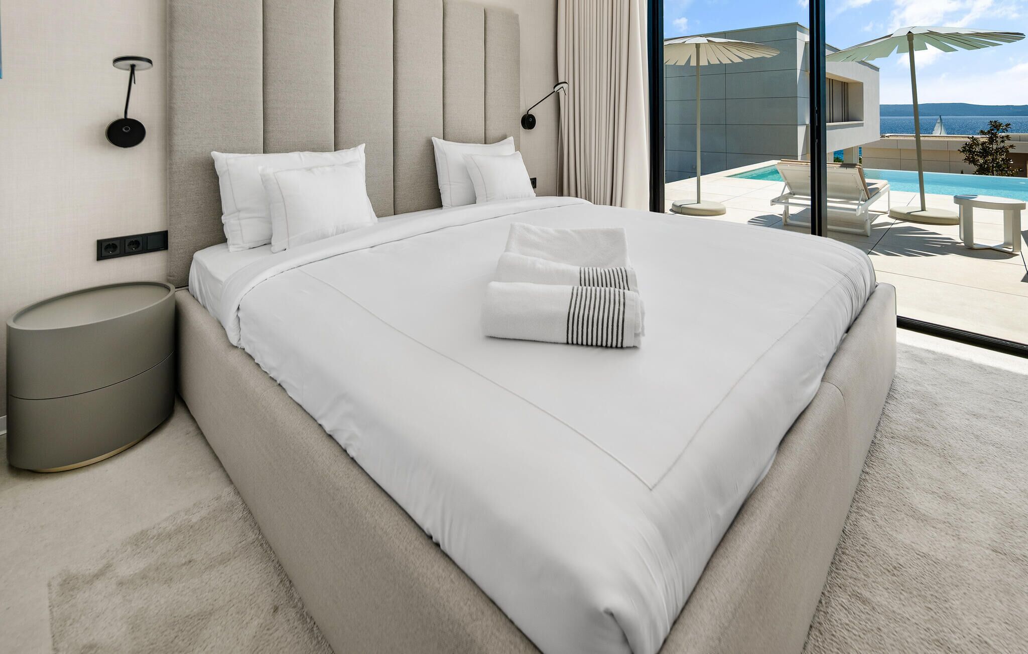 Habitación de hotel moderna con una cama grande, una mesita de noche, vista a una piscina y al mar.