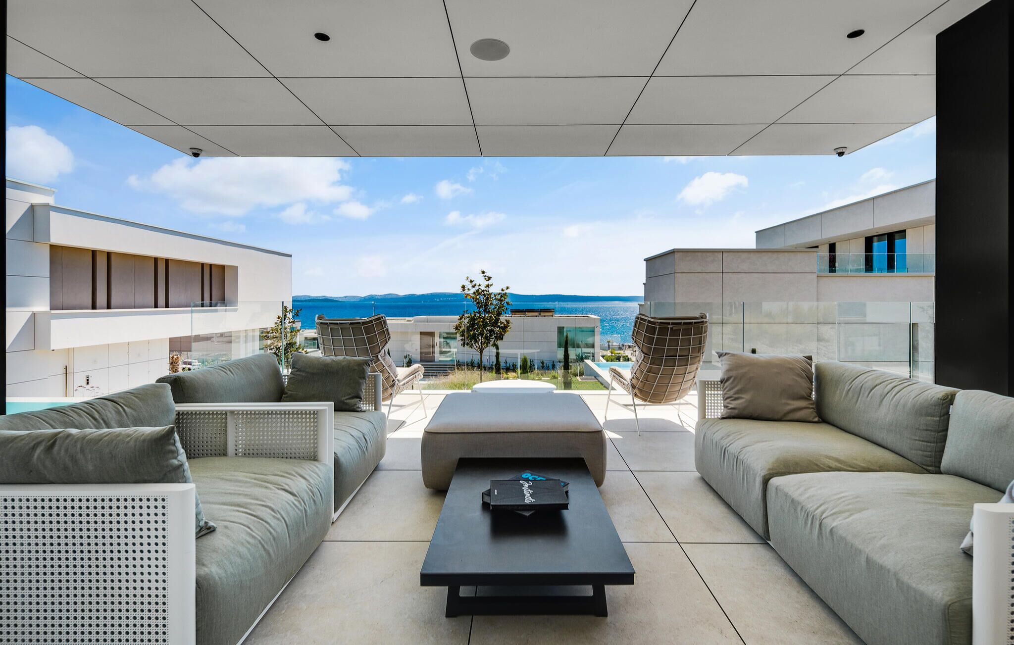 Un espacio exterior moderno con vistas al mar, que incluye un sofá, una mesa de centro y una partición de vidrio.