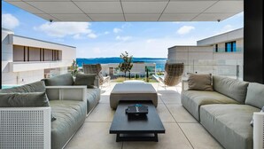 Ein moderner Außenbereich mit Meerblick, ausgestattet mit einer Couch, einem Couchtisch und einer Glasscheibe.