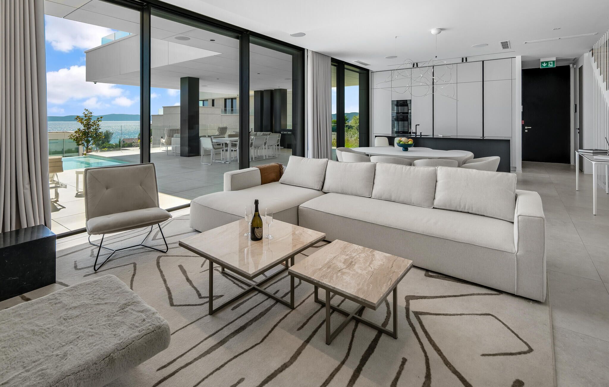 A modern living room with a sectional sofa, a glass coffee table, and a view of the pool and outdoor seating area.