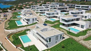 Ein moderner Wohnkomplex mit mehreren zweistöckigen Häusern, jedes mit einem Schwimmbad und Solaranlage.