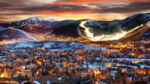 Une vue panoramique d’une ville enneigée, avec des bâtiments illuminés et des montagnes en arrière-plan.