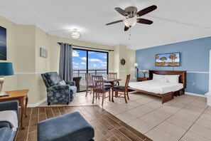 Ein Hotelzimmer mit Bett, Esstisch mit Stühlen, einem Balkon mit Aussicht und einem Deckenventilator.