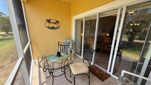 Ein Balkon mit Glastür, die in ein Wohnzimmer führt, ein kleiner Tisch mit Stühlen und eine Wanddekoration im tropischen Stil.