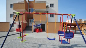 Ein Spielplatz mit Schaukeln und einer Rutsche vor einem Gebäude mit mehreren Balkonen.