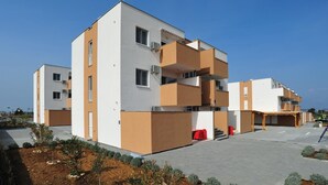 Un immeuble résidentiel moderne à plusieurs étages, doté de balcons, d’un espace extérieur couvert aménagé en coin salon et d’une cour pavée.