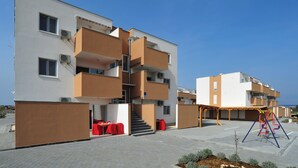Un immeuble d’appartements moderne doté de nombreux balcons, d’un espace extérieur couvert avec des tables et d’un terrain de jeux.