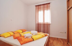 Ein Einzelbett mit vielen Kissen und zusammengerollten Handtüchern, ein Fenster mit Vorhängen und eine Holztür.