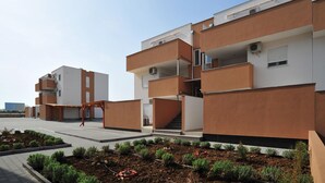 Ein modernes, mehrgeschossiges Wohngebäude mit Balkonen, einer überdachten Außenfläche und einem angelegten Garten.