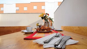 Ein Frühstücksangebot auf einem Holztisch mit Croissants, einer Blumenvase und einer Gebäudeblick im Hintergrund.