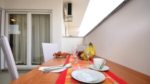 Taula de menjador preparada amb croissants, glops de vi i un plat de fruita a un balcó amb vista al cel.