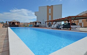 Une piscine rectangulaire bordée de blanc, entourée de chaises longues et d’une pergola.