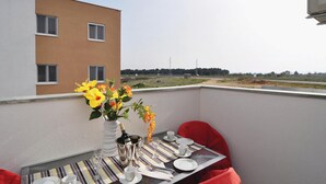 A balcony with a dining table set for two, a vase with flowers, and a view of a building and distant power lines.