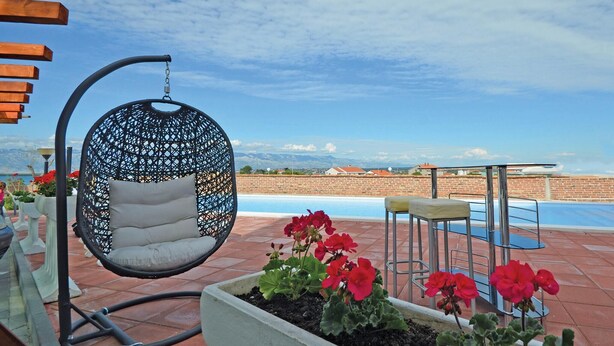 A hanging chair with a cushion, a pool, and red flowers in a planter. - Lovely apartment in Nin with WiFi (Nin)