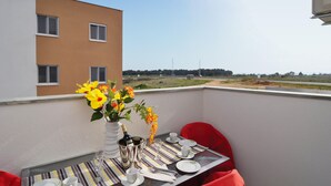 A balcony with a table set for two, a vase of flowers, and a bottle of champagne. The balcony overlooks a building and a distant landscape. - Lovely apartment in Nin with WiFi (Nin)