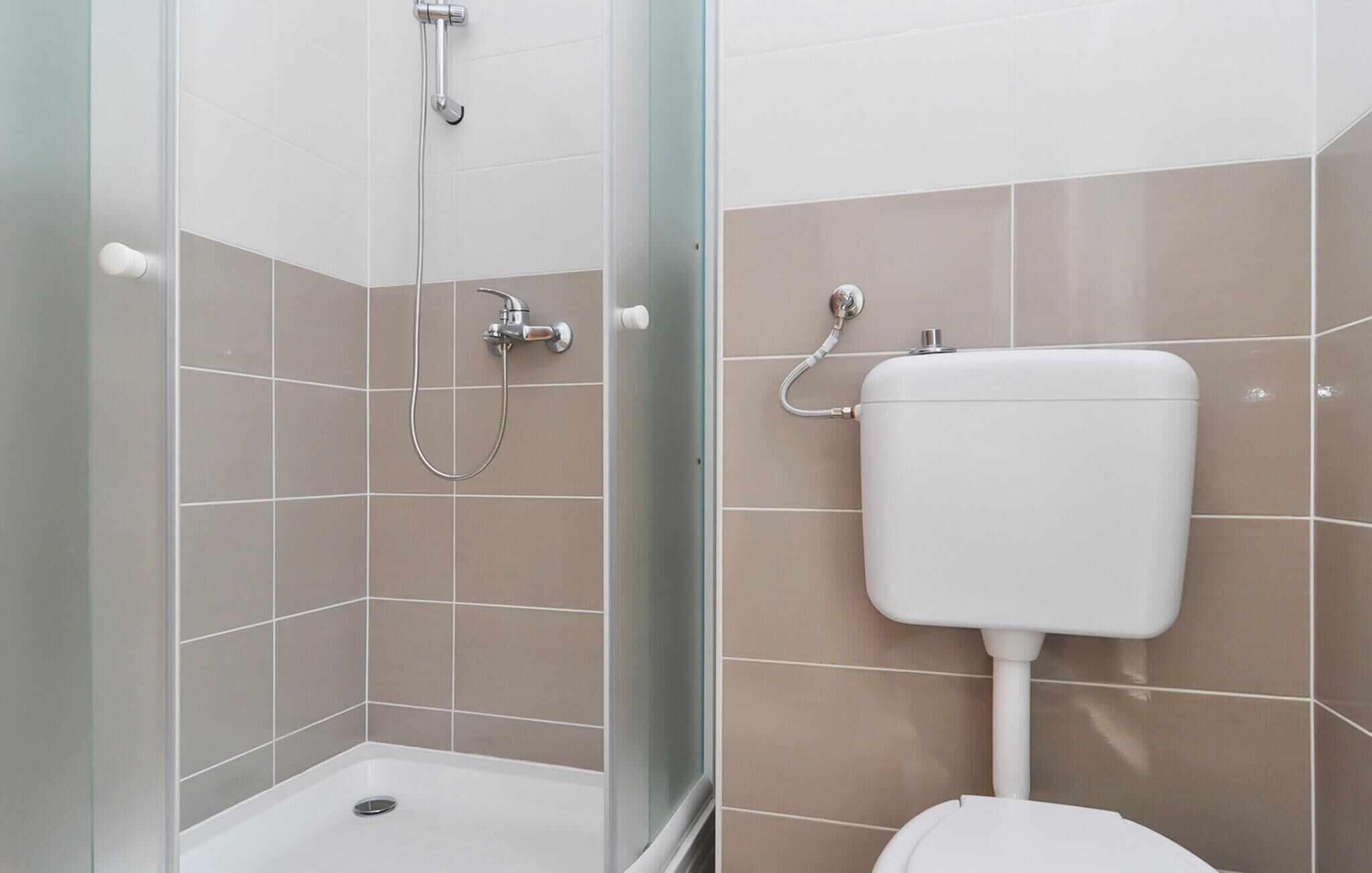 Un baño con ducha, inodoro y zona de ducha con mampara de vidrio.