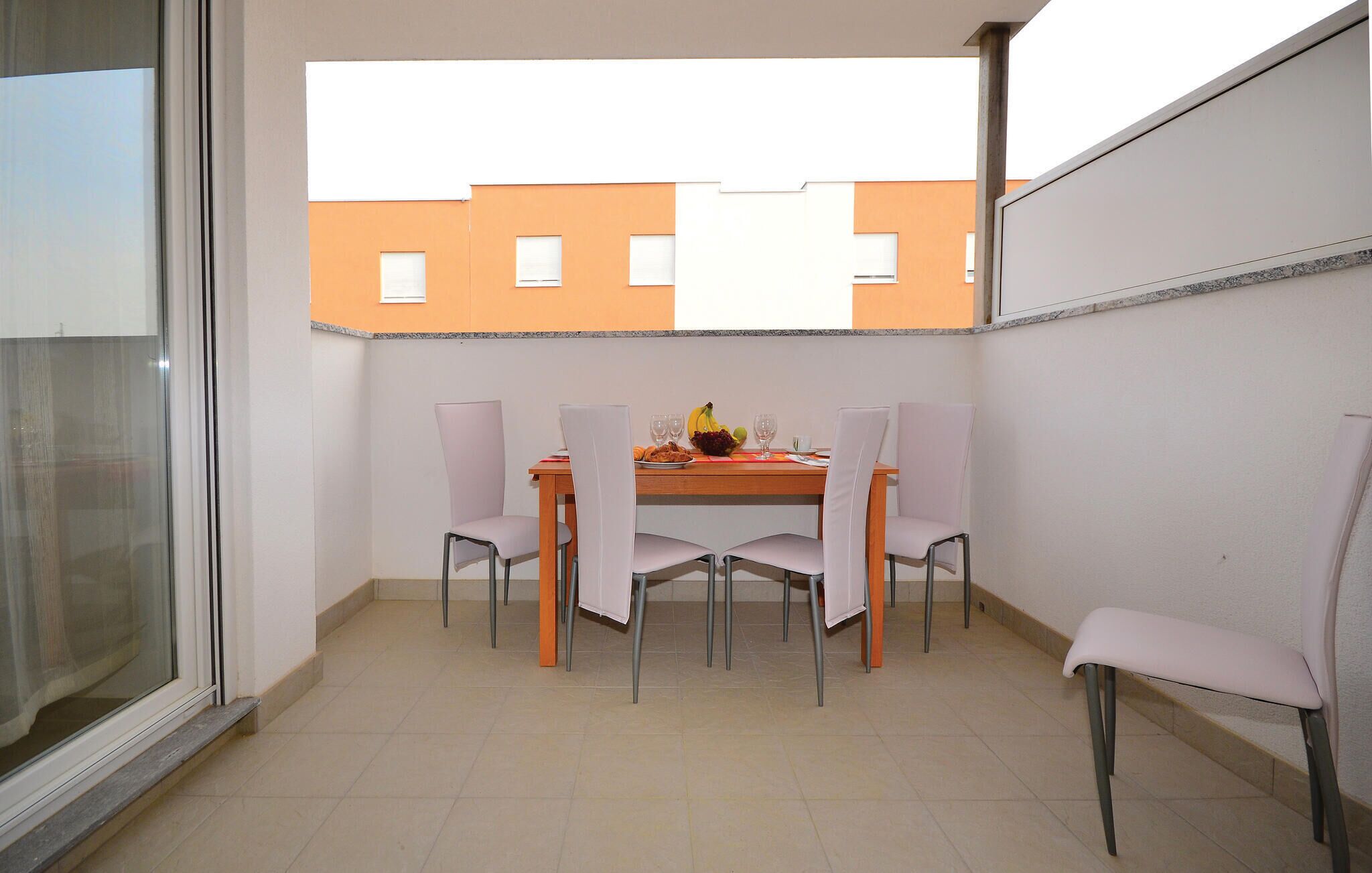 A balcony with a dining table, four chairs, and a fruit bowl.