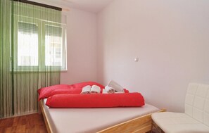Ein Zimmer mit einem Einzelbett, einem hölzernen Bettgestell, einer weißen Matratze, roten Kissen und einem weißen Nachttisch.