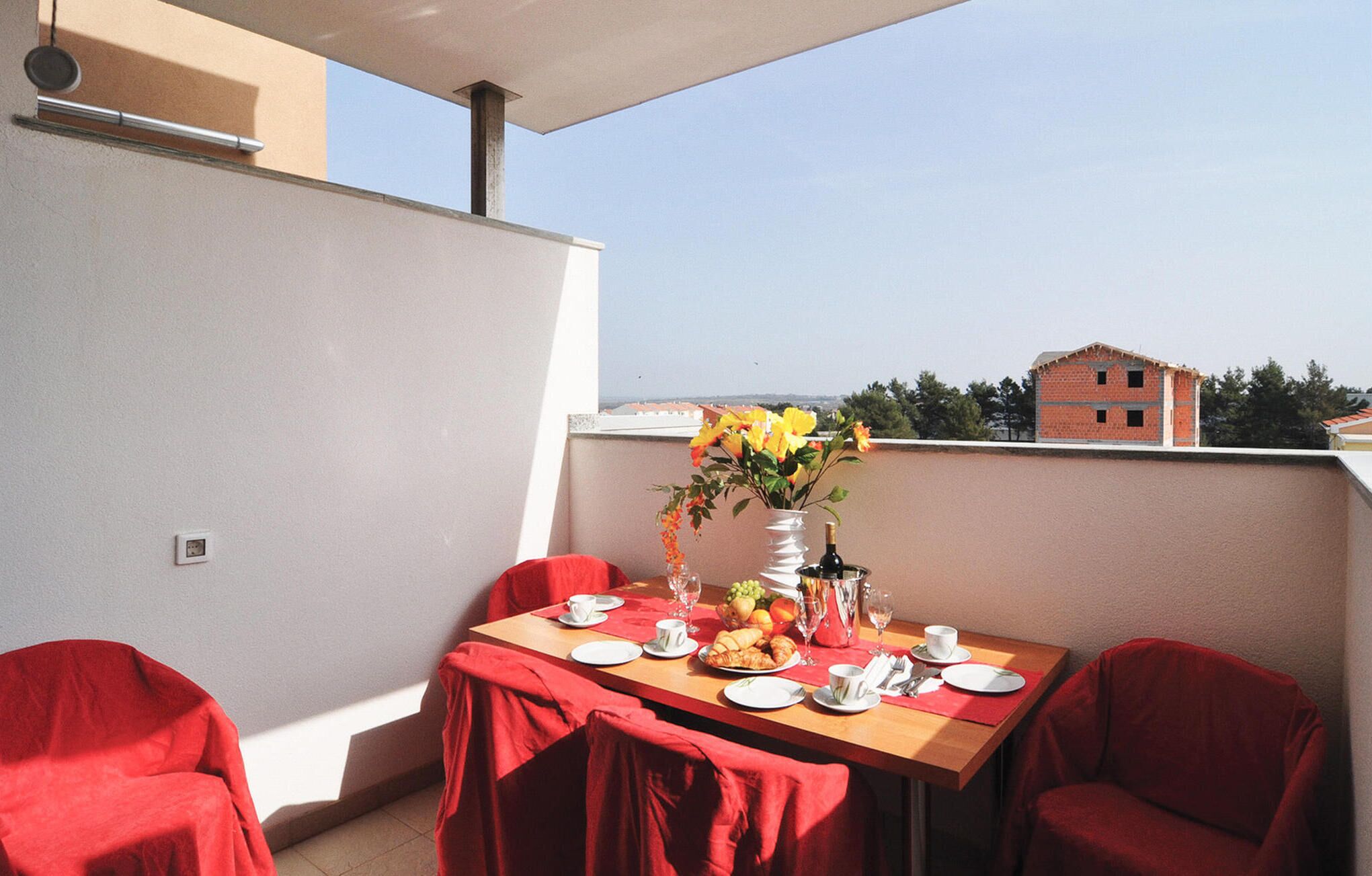 A dining area with a table set for two, a vase with flowers, and a view of buildings in the background.