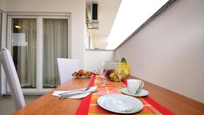 Et spisebord dækket med croissanter, frugt, vinglas og tallerkener, med udsigt til en bygning og et vindue i baggrunden.
