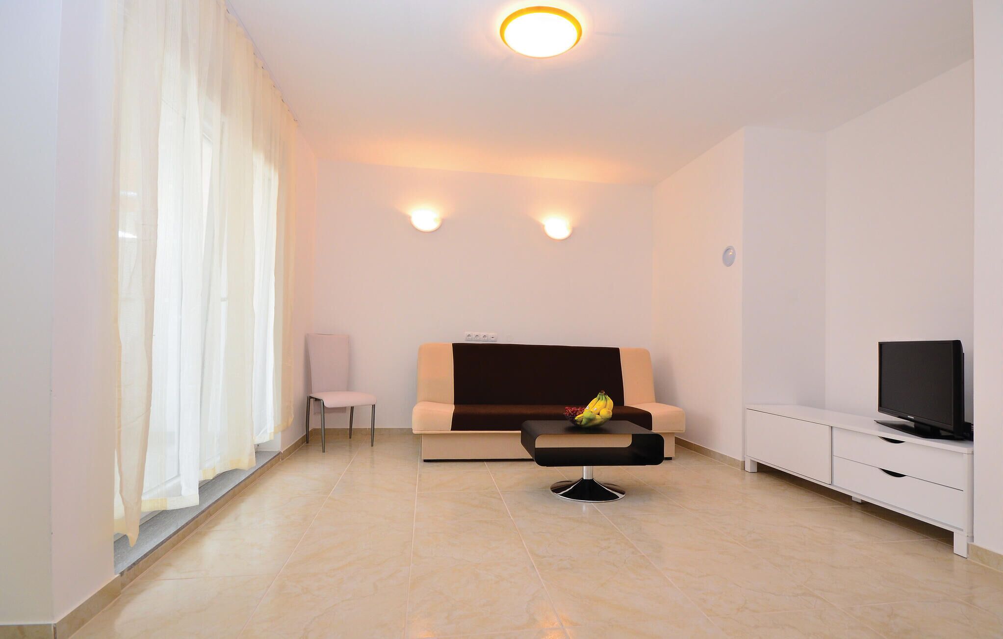 A modern living room with a sofa, a small table with fruit, a TV, and a chair.