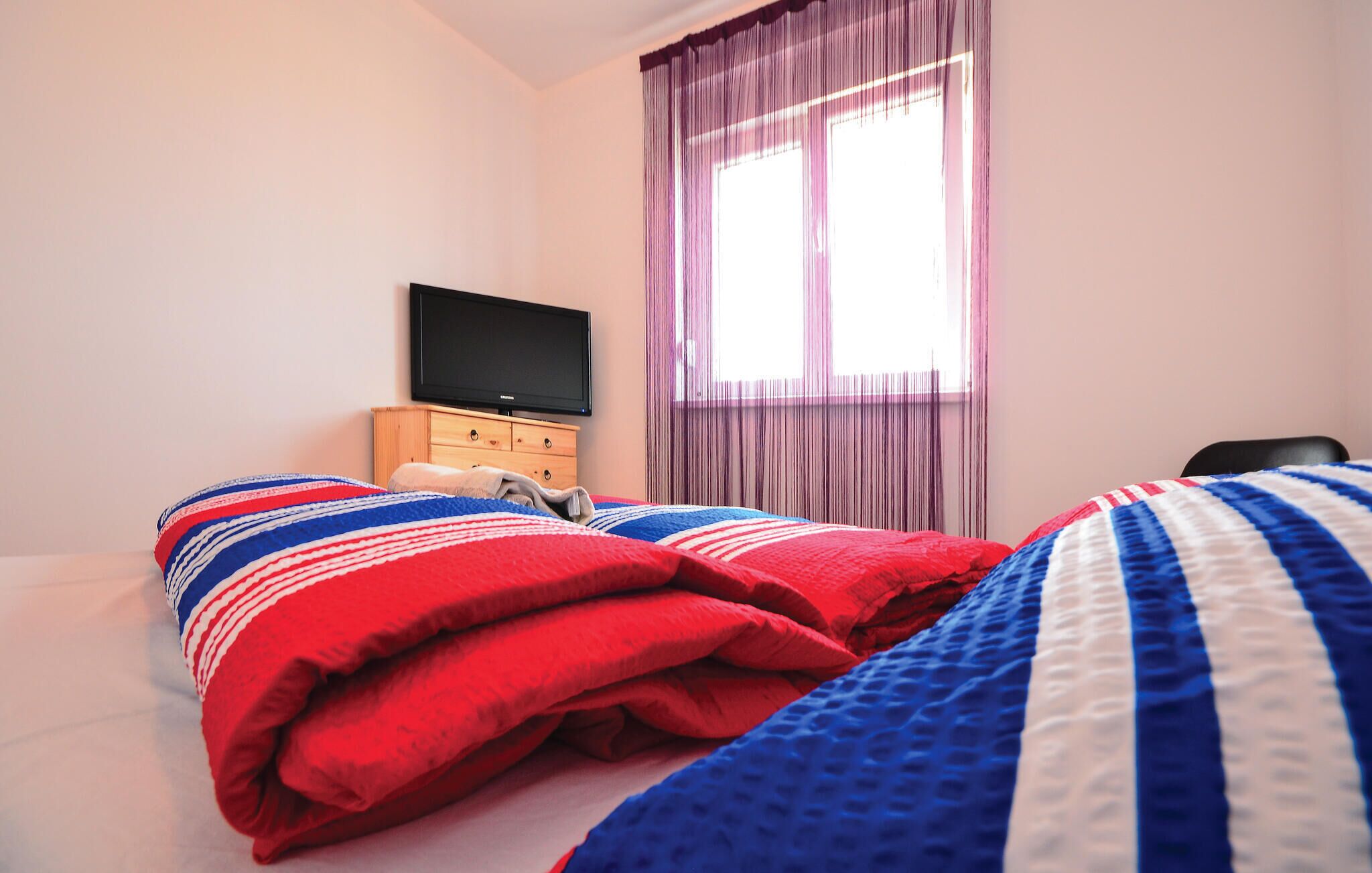 A hotel room with a bed, a TV, a wooden dresser, and a window with curtains.