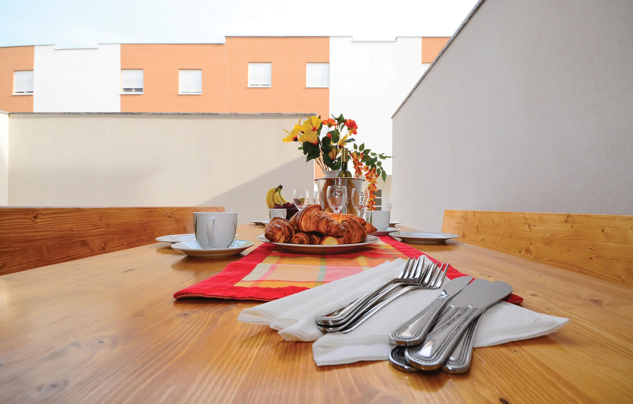 A breakfast table with croissants, a cup, and a vase with flowers.