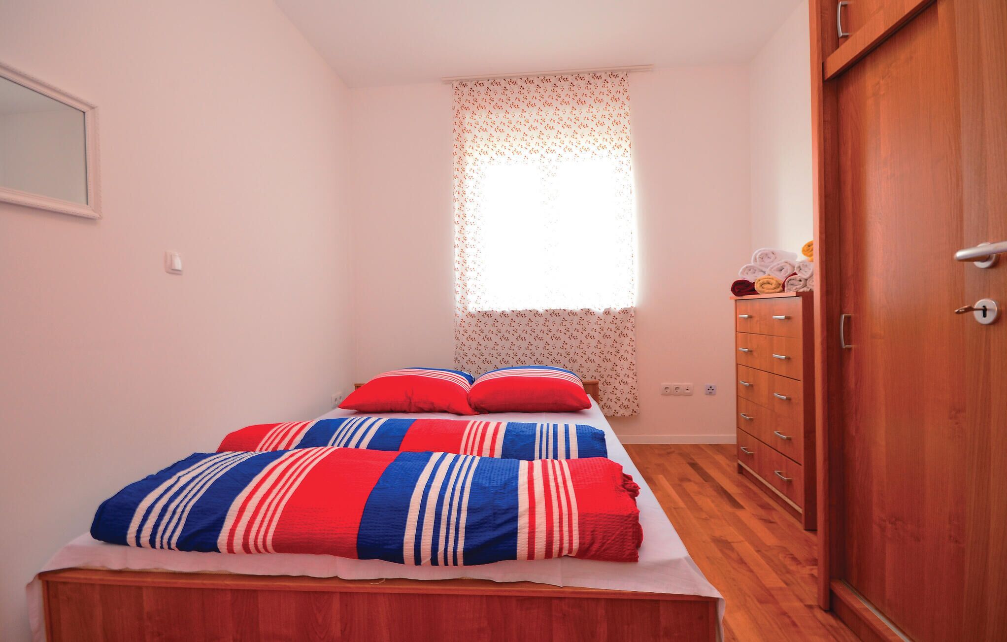 A bedroom with a bed, a wooden wardrobe, and a window with floral curtains.