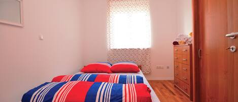 A bedroom with a bed, a wooden wardrobe, and a window with floral curtains.