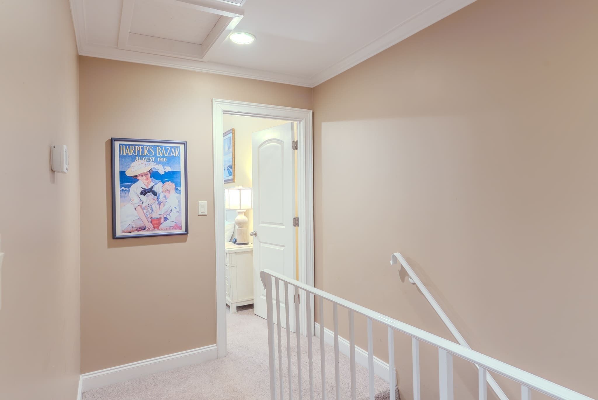 A hallway with beige walls, a white door, and a staircase with white railings.