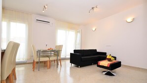 Una sala de estar moderna con comedor, que presenta un sofá negro, una mesa de vidrio y un pequeño taburete negro con un cuenco de frutas.