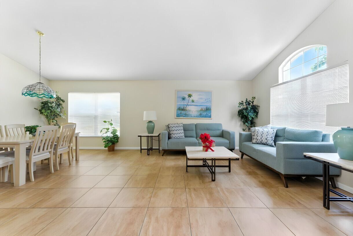 A spacious living room with a dining area, a light blue sofa, a coffee table, and a painting of a beach scene.
