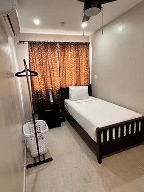 A small, neatly arranged bedroom with a single bed, a nightstand, a hanging light, a laundry basket, and a ceiling fan. - Celestial Suite- 3Bedroom Belize City (Belize City)