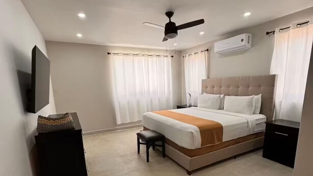 Une chambre d’hôtel moderne dotée d’un grand lit, d’un ventilateur de plafond, d’un appareil de climatisation et d’un téléviseur à écran plat fixé au mur.