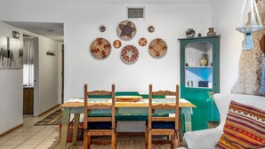 A dining area with a wooden table and chairs, a green cabinet with shelves, and a wall decorated with various plates. - Cielo Grande · Near Santa Fe Plaza, Small Fenced Yard, Parking (Santa Fe)