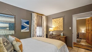 A bedroom with a bed, a nightstand, a lamp, and a wall with a tapestry and a mirror. - Cielo Grande · Near Santa Fe Plaza, Small Fenced Yard, Parking (Santa Fe)