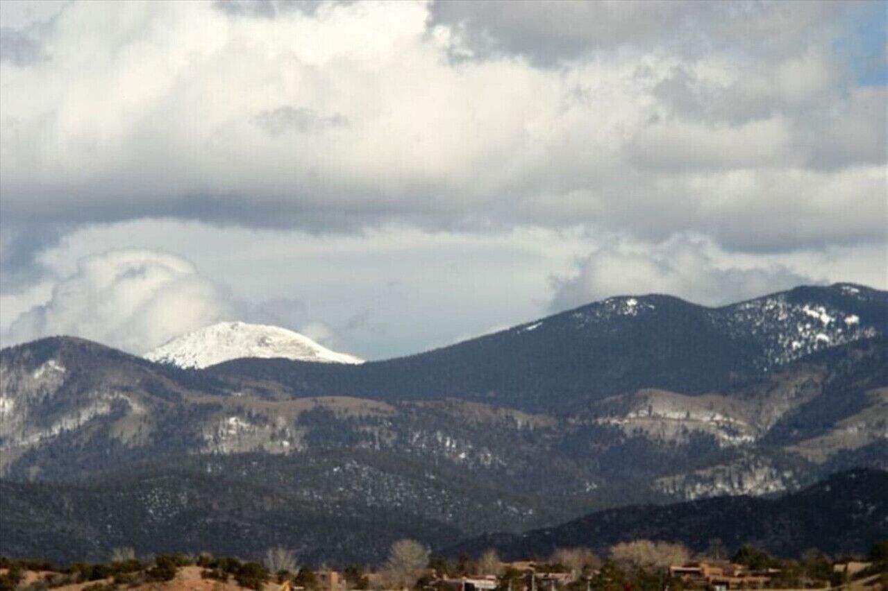 A mountainous landscape with snow-capped peaks and a cloudy sky.
