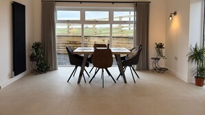 Ein Essbereich mit Tisch und Stühlen, Blick auf einen Holzzaun und Grünanlagen im Freien sowie ein Heizkörper links.