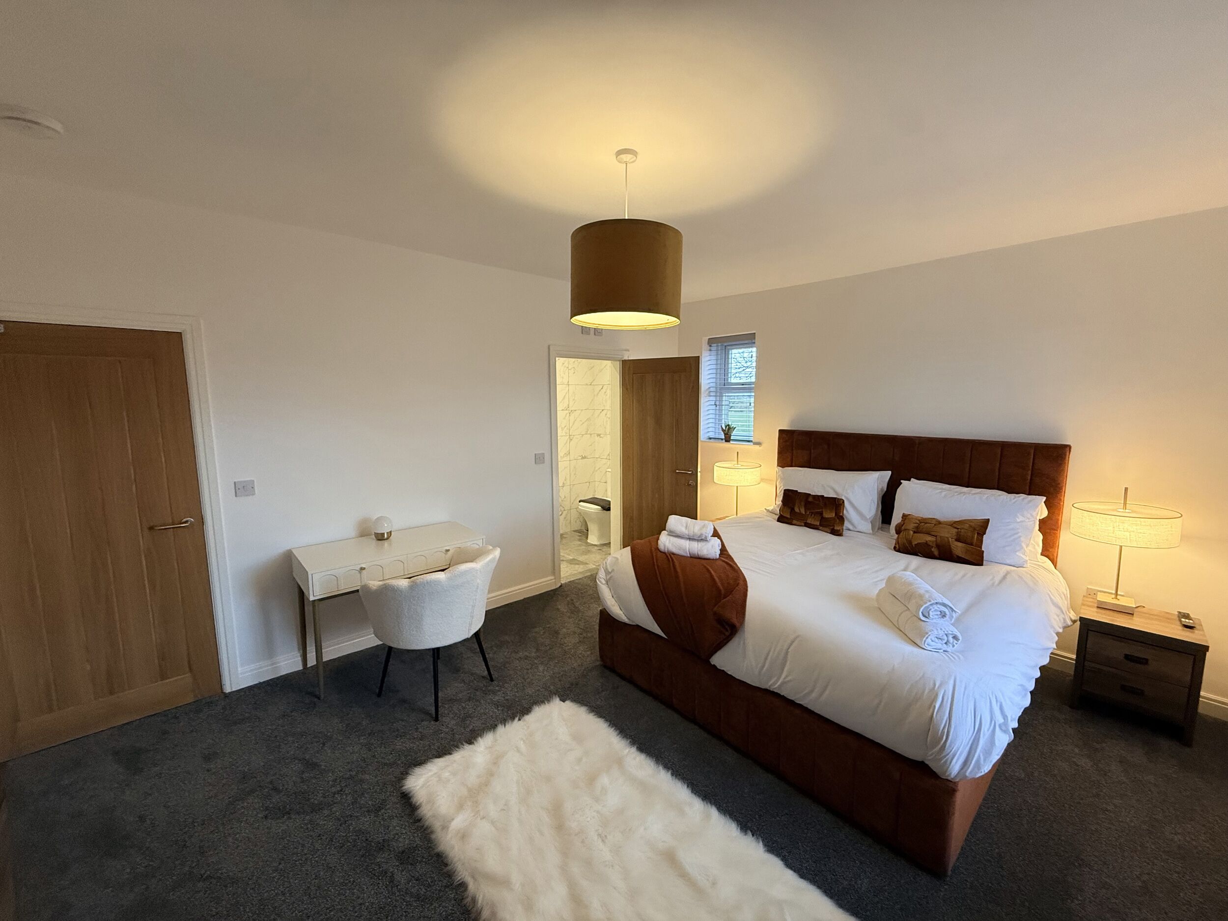 A bedroom with a large bed, bedside tables, a desk, and a chair.