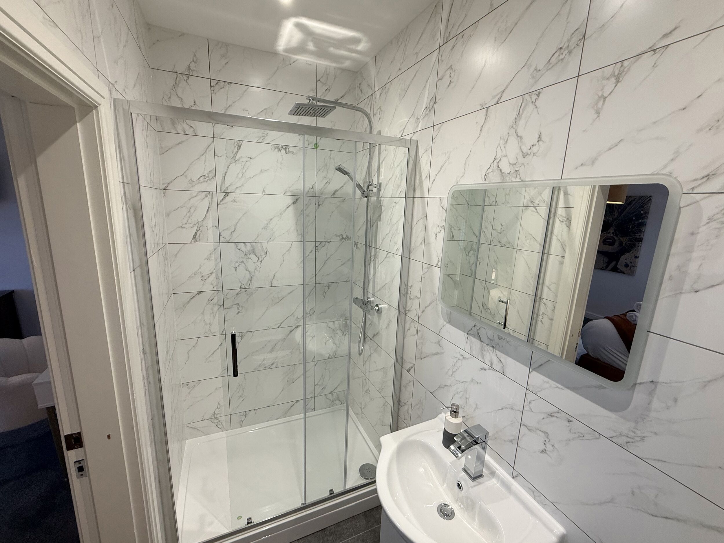 Ein modernes Badezimmer mit einer Glaskabine zur Dusche, einem Waschbecken mit Spiegel und Wänden mit Marmormuster.