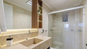 A modern bathroom with a glass shower enclosure, a marble sink, and a wooden medicine cabinet with LED lighting. - Apartments in Beachfront Condo in Itapema - DNL (Itapema)